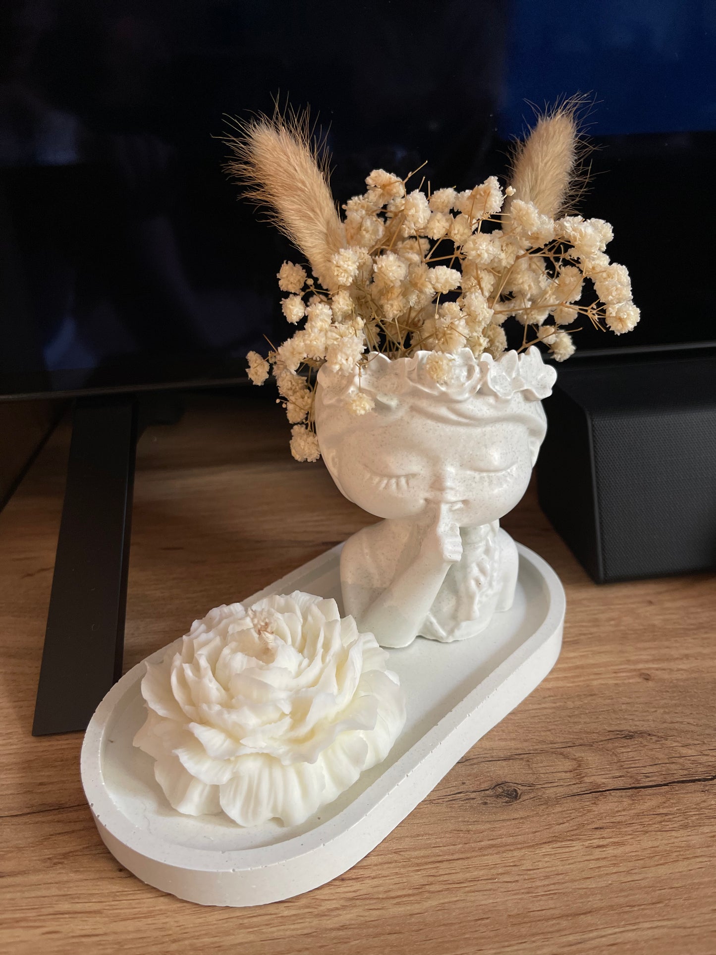 Minimalistische Betonvase mit Trockenblumen und brennender Duftkerze als stilvolle Wohnraumdekoration auf einem Regal im Wohnzimmer in der Farbe Beige/ Creme